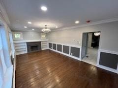 unfurnished living room with an inviting chandelier, ornamental molding, and dark hardwood / wood-style flooring