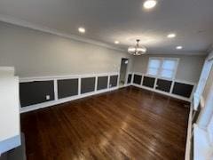 spare room with a notable chandelier, dark wood-type flooring, and ornamental molding