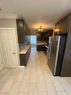 kitchen with crown molding, dark brown cabinets, and stainless steel refrigerator