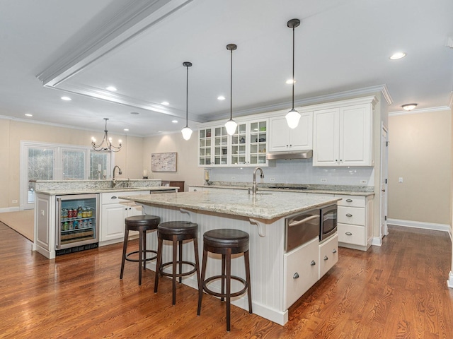 kitchen with wine cooler, white cabinetry, a kitchen island with sink, and pendant lighting