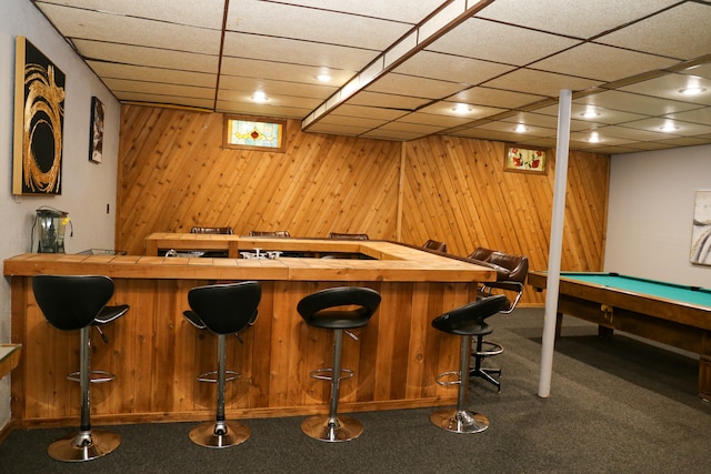 bar featuring dark colored carpet, wooden walls, pool table, and a drop ceiling