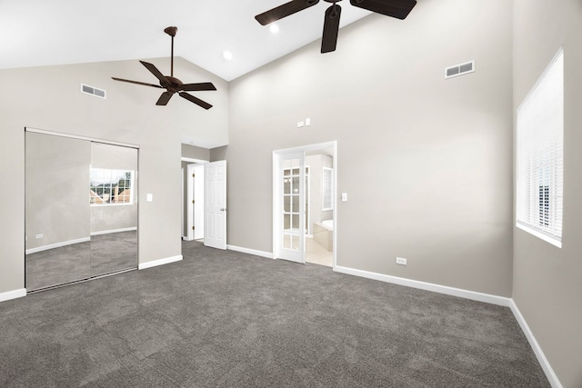 unfurnished bedroom featuring ceiling fan, high vaulted ceiling, dark carpet, ensuite bathroom, and a closet