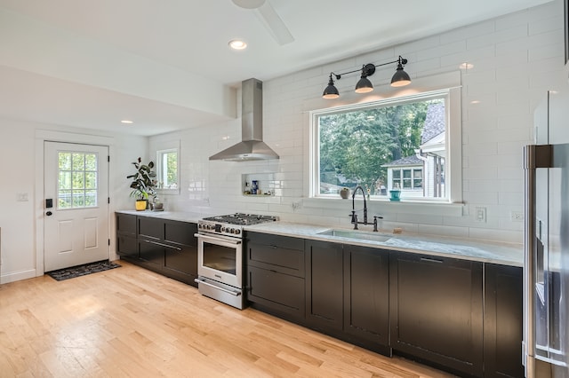 kitchen with appliances with stainless steel finishes, sink, plenty of natural light, wall chimney exhaust hood, and light hardwood / wood-style flooring