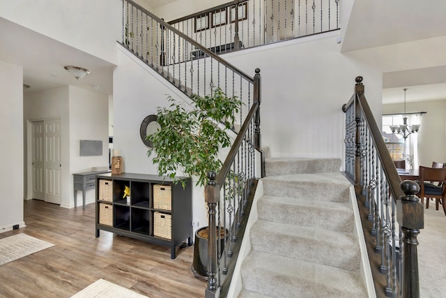 stairway featuring a towering ceiling, hardwood / wood-style flooring, and a chandelier