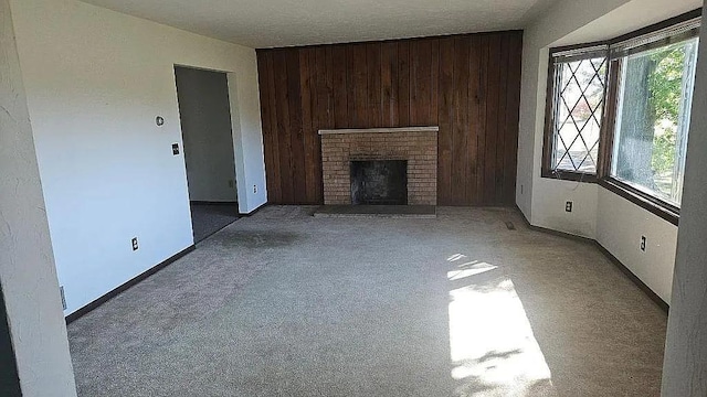 unfurnished living room featuring carpet floors, a healthy amount of sunlight, wooden walls, and a fireplace