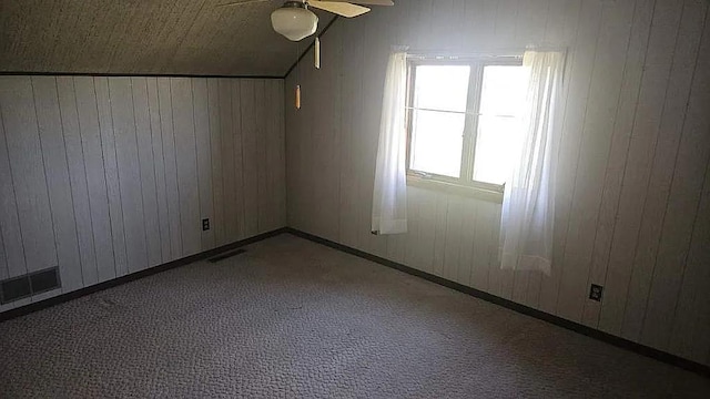 carpeted spare room featuring ceiling fan, lofted ceiling, and wooden walls