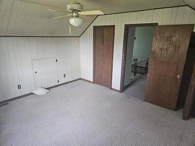 unfurnished bedroom featuring ceiling fan, wood walls, carpet, and lofted ceiling