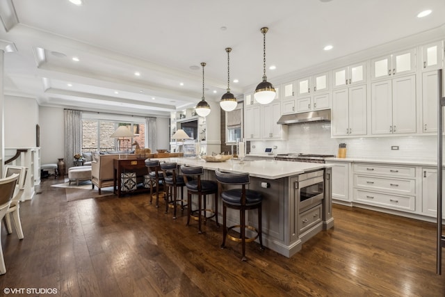 kitchen with a kitchen island with sink, stainless steel microwave, dark wood-type flooring, pendant lighting, and white cabinets