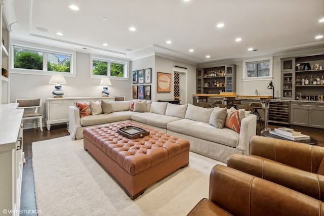 living room featuring wine cooler, ornamental molding, bar, and light wood-type flooring