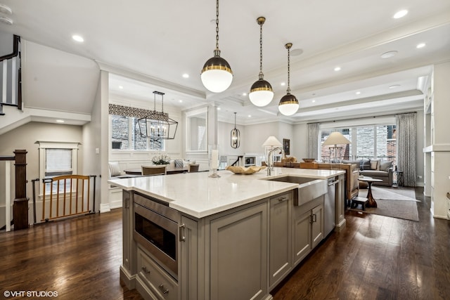 kitchen with stainless steel appliances, decorative light fixtures, gray cabinets, dark wood-type flooring, and a center island with sink