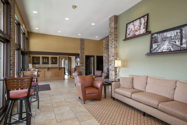 living area featuring a towering ceiling, brick wall, and light tile patterned floors