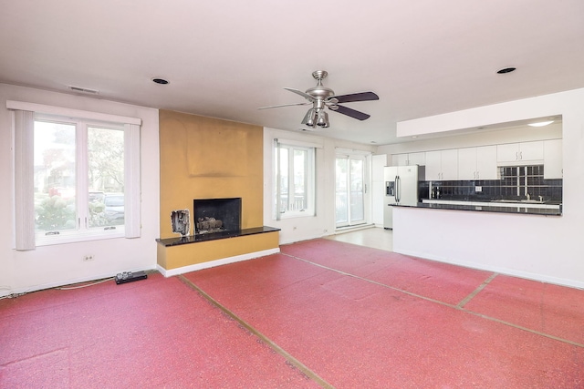 unfurnished living room with baseboards, visible vents, a ceiling fan, light colored carpet, and a fireplace