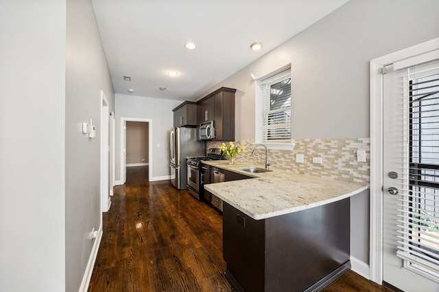 kitchen featuring appliances with stainless steel finishes, sink, backsplash, dark brown cabinets, and dark wood-type flooring