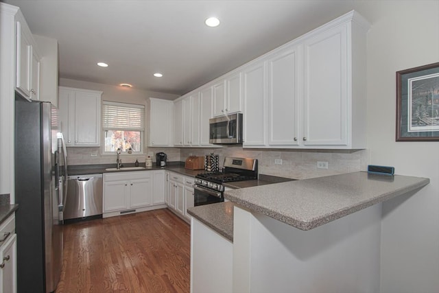 kitchen featuring dark hardwood / wood-style floors, kitchen peninsula, stainless steel appliances, sink, and white cabinetry