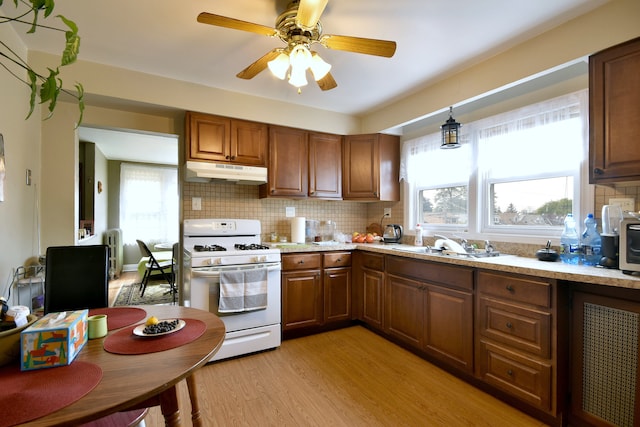 kitchen with decorative backsplash, light hardwood / wood-style floors, a healthy amount of sunlight, and gas range gas stove