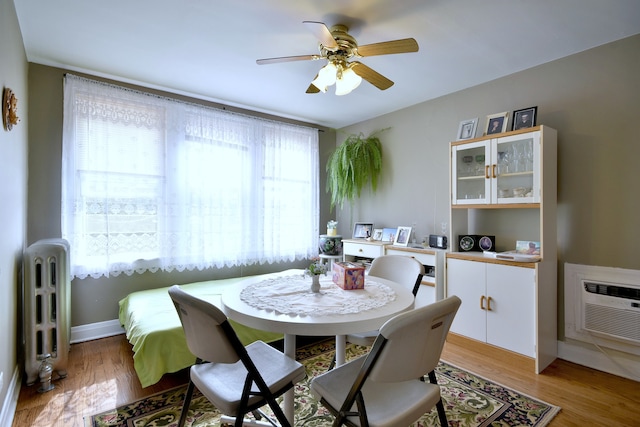 dining area with ceiling fan, an AC wall unit, radiator heating unit, and light wood-type flooring