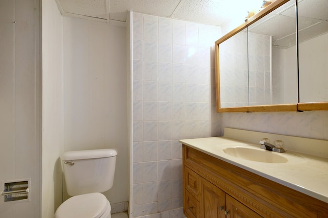 bathroom featuring toilet, walk in shower, vanity, and tile walls