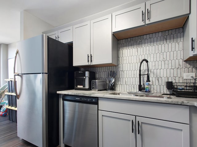 kitchen with dark wood-type flooring, sink, light stone countertops, white cabinets, and appliances with stainless steel finishes