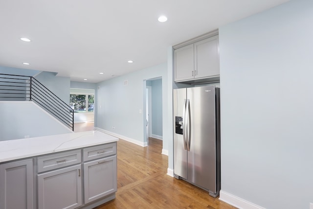 kitchen featuring light stone counters, stainless steel fridge with ice dispenser, light wood-type flooring, and gray cabinets