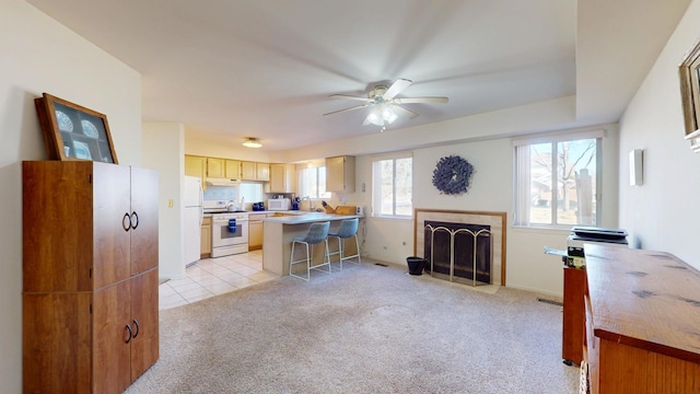 kitchen with a kitchen bar, white appliances, light colored carpet, kitchen peninsula, and ceiling fan