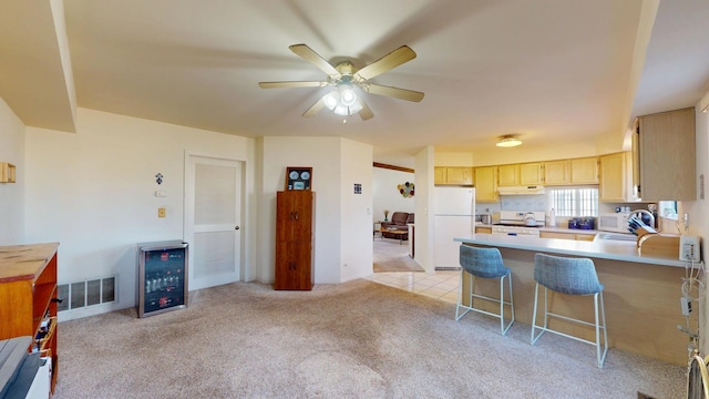 kitchen featuring wine cooler, light brown cabinetry, sink, a breakfast bar area, and white appliances