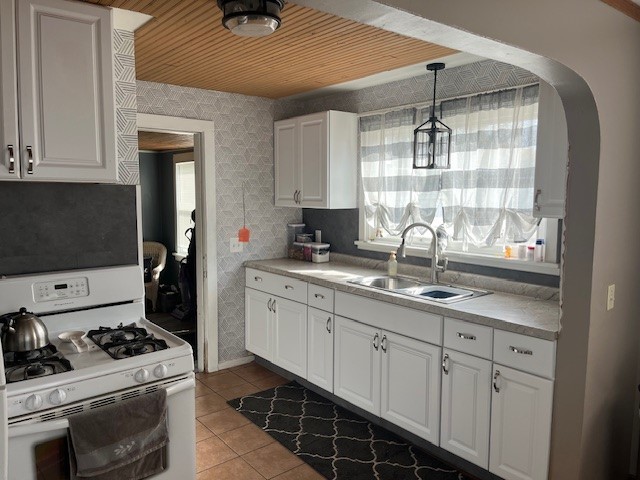 kitchen featuring white gas range oven, sink, decorative light fixtures, and white cabinets