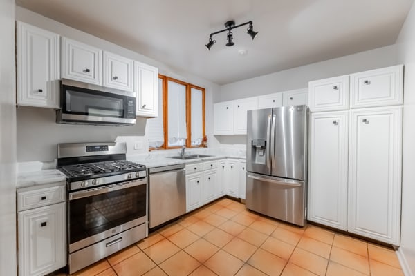 kitchen with sink, appliances with stainless steel finishes, light tile patterned floors, and white cabinets