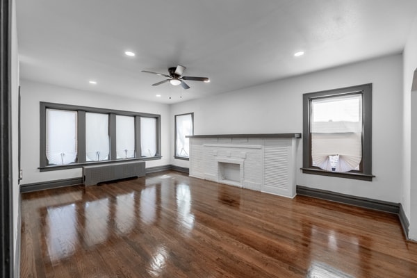 unfurnished living room featuring radiator, ceiling fan, a stone fireplace, and dark hardwood / wood-style flooring