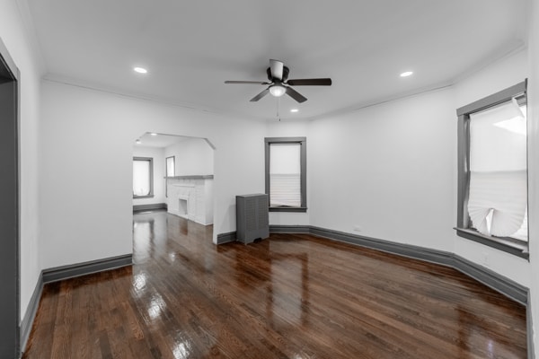 unfurnished living room with dark wood-type flooring, ceiling fan, and crown molding