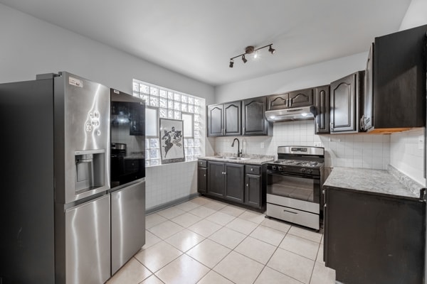 kitchen with decorative backsplash, dark brown cabinets, stainless steel appliances, sink, and light tile patterned floors