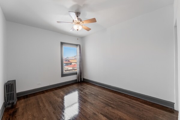 spare room featuring ceiling fan, radiator heating unit, and dark hardwood / wood-style flooring