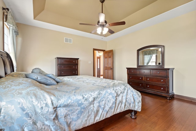 bedroom featuring ceiling fan, a tray ceiling, and dark hardwood / wood-style flooring