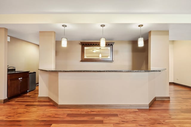 kitchen with stone counters, light hardwood / wood-style flooring, kitchen peninsula, and pendant lighting