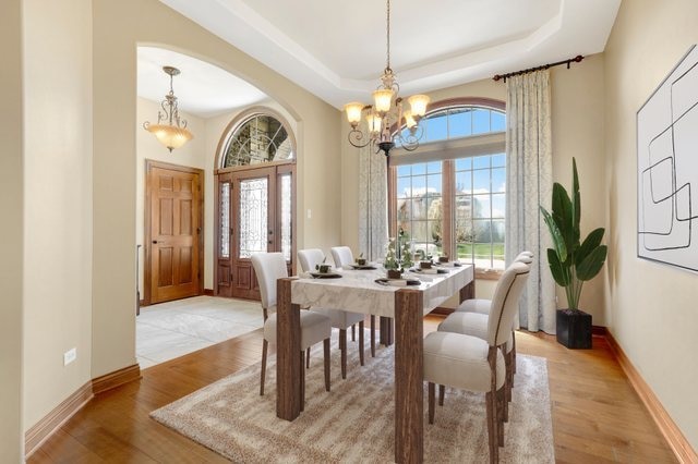 dining room with a wealth of natural light, light hardwood / wood-style flooring, a notable chandelier, and a raised ceiling