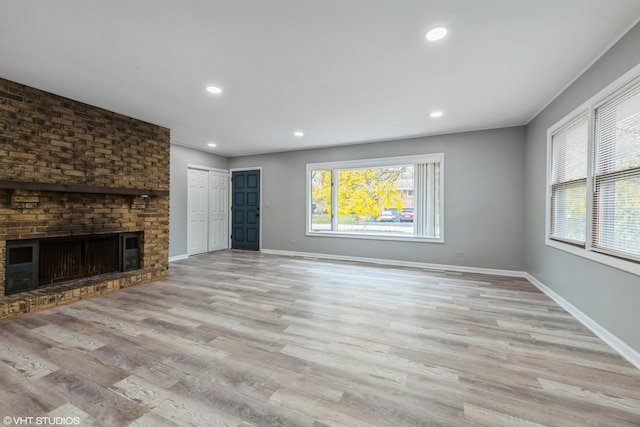 unfurnished living room featuring light hardwood / wood-style flooring, a wealth of natural light, and a brick fireplace