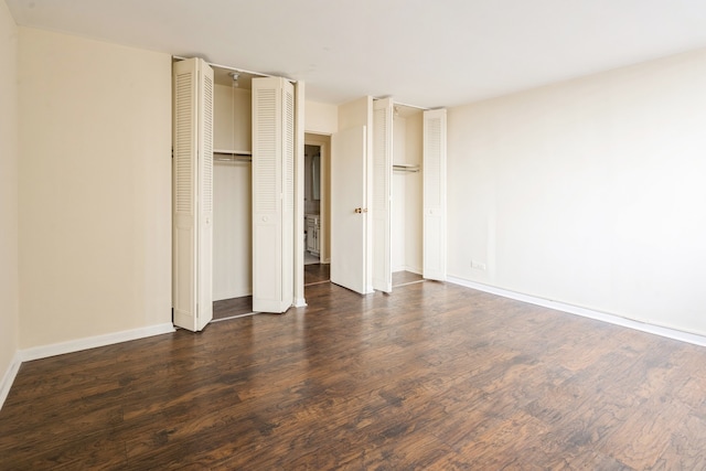 unfurnished bedroom with two closets and dark hardwood / wood-style floors