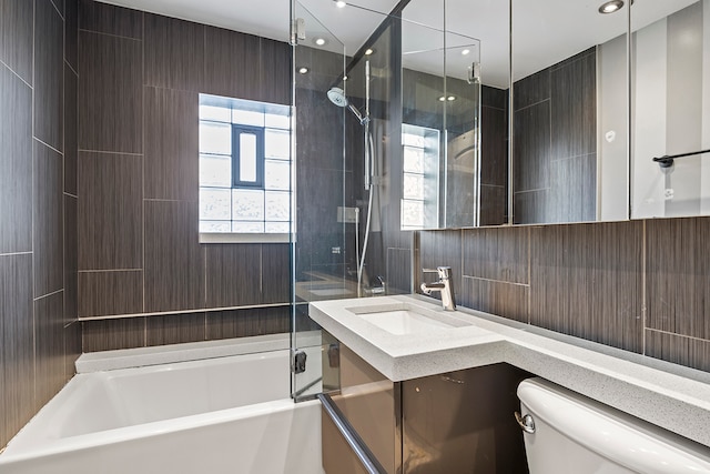 full bathroom featuring tile walls, vanity, tiled shower / bath combo, and toilet