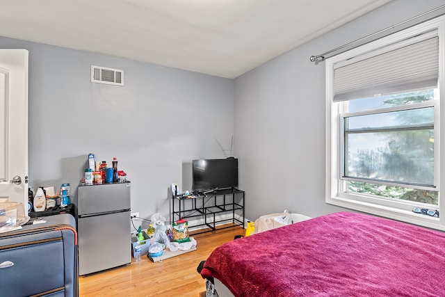 bedroom featuring stainless steel fridge, multiple windows, and hardwood / wood-style flooring