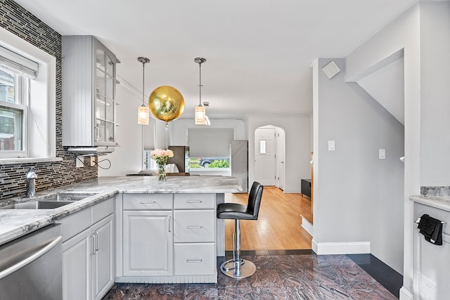 kitchen with kitchen peninsula, hanging light fixtures, a breakfast bar area, white cabinetry, and stainless steel dishwasher