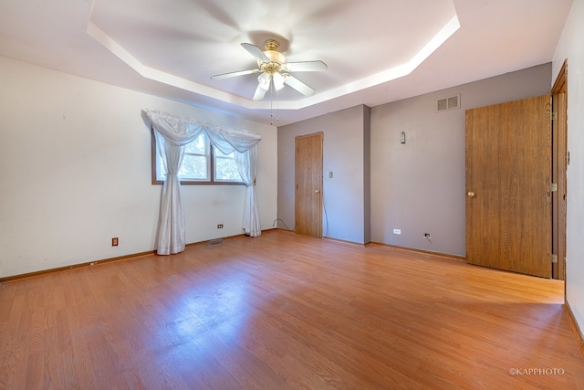 empty room with light hardwood / wood-style floors, a tray ceiling, and ceiling fan