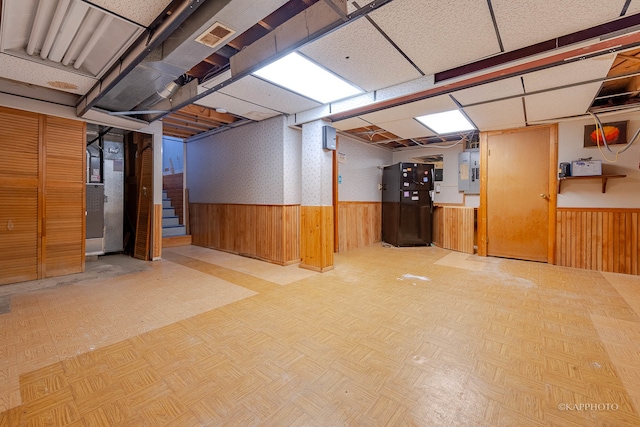 basement featuring wooden walls, electric panel, light parquet flooring, and black fridge