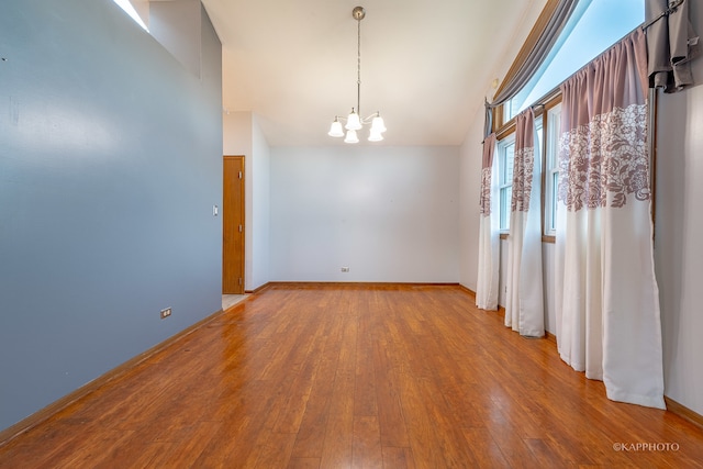 empty room featuring a notable chandelier, wood-type flooring, and lofted ceiling