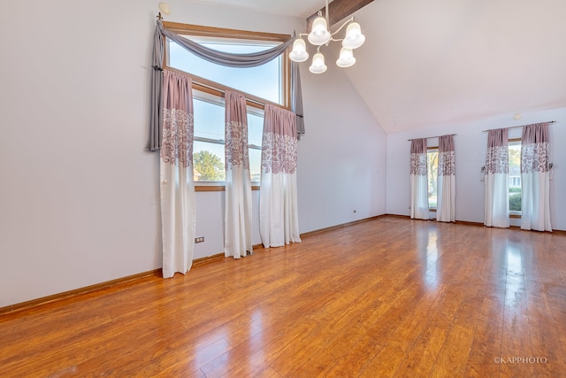 empty room featuring an inviting chandelier, hardwood / wood-style flooring, and high vaulted ceiling