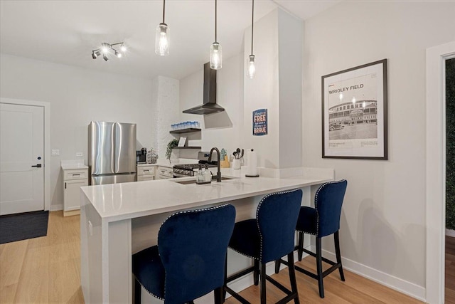 kitchen featuring light wood-style flooring, a sink, appliances with stainless steel finishes, wall chimney exhaust hood, and a peninsula