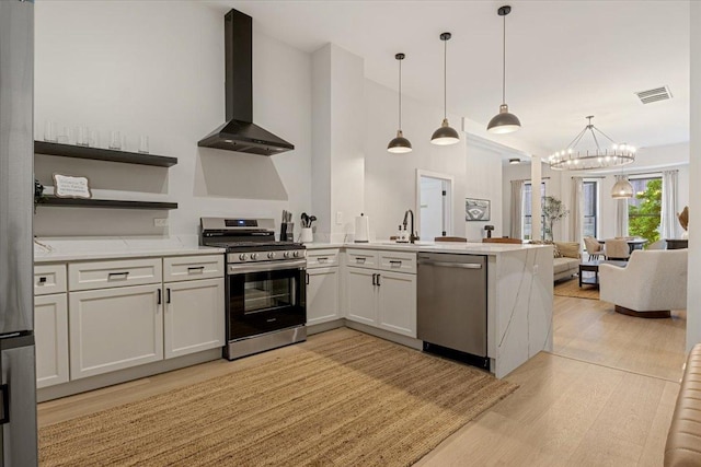kitchen featuring gas range, wall chimney exhaust hood, light stone counters, and a sink