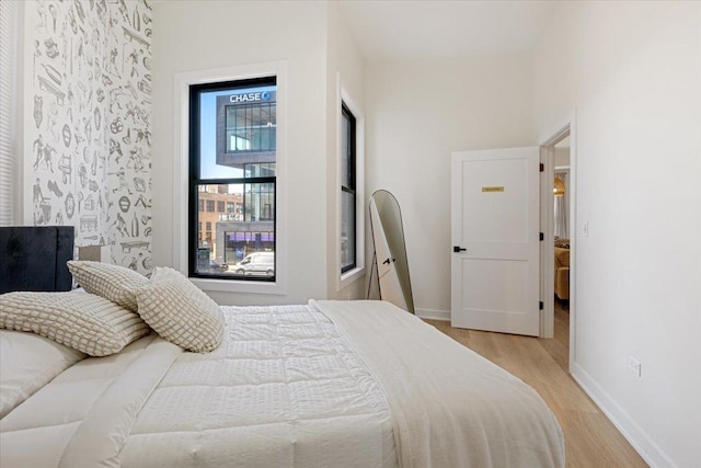 bedroom with wallpapered walls, wood finished floors, and baseboards