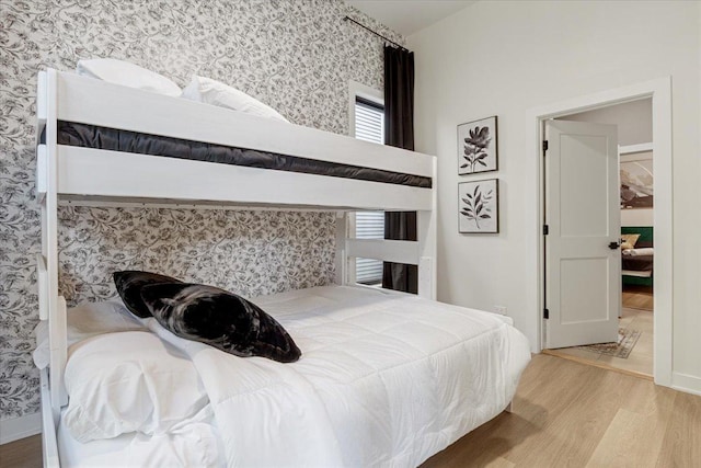 bedroom featuring wallpapered walls, wood finished floors, and baseboards
