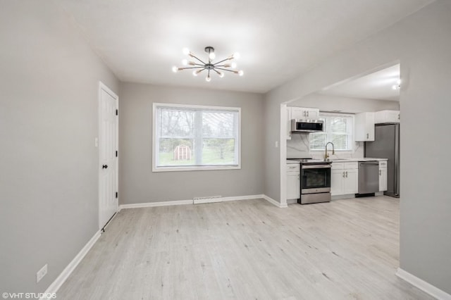 kitchen with light wood-type flooring, appliances with stainless steel finishes, white cabinetry, and a healthy amount of sunlight