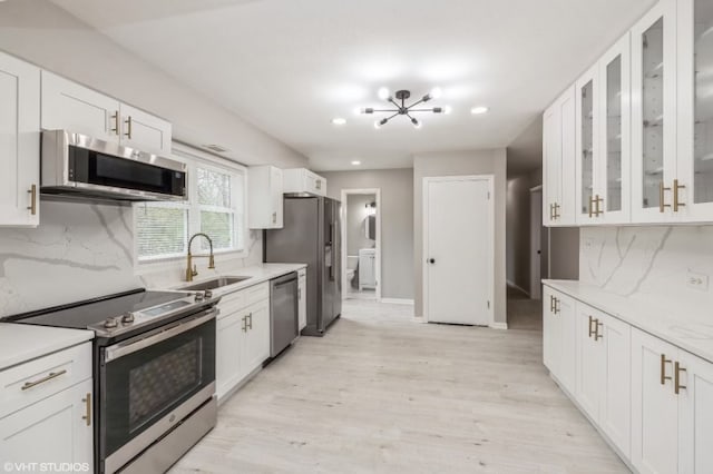 kitchen with tasteful backsplash, appliances with stainless steel finishes, sink, white cabinetry, and light hardwood / wood-style flooring