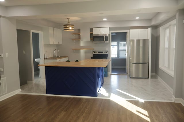 kitchen featuring white cabinetry, stainless steel appliances, butcher block countertops, hardwood / wood-style floors, and decorative light fixtures